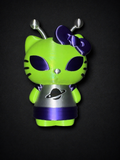 Close front view of the green Alien Hello Kitty figure with purple bow and eyes, silver antennae and dress, and black planet emblem.