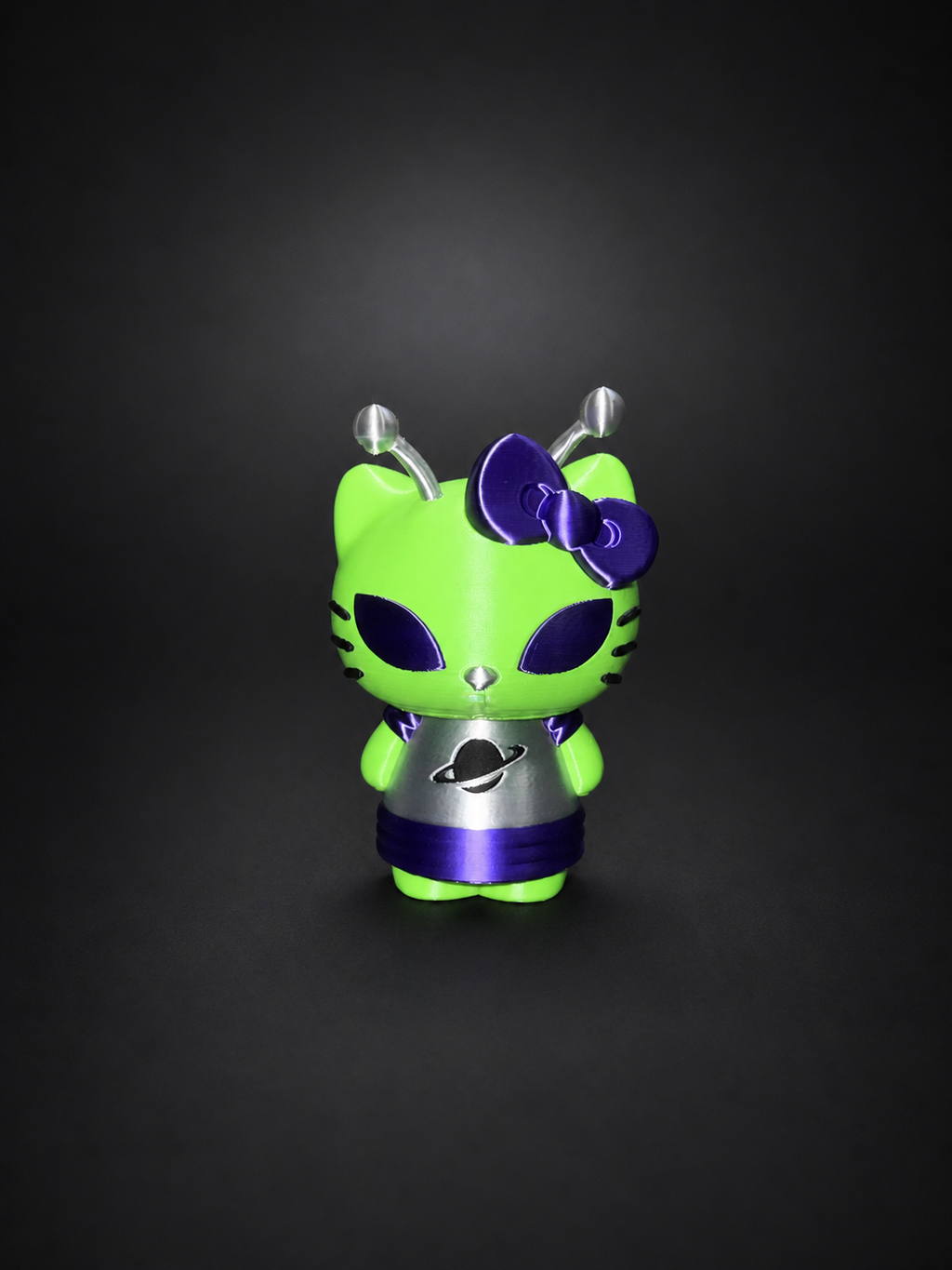 Full view of the green, purple, silver, and black Alien Hello Kitty display figure against a dark background.