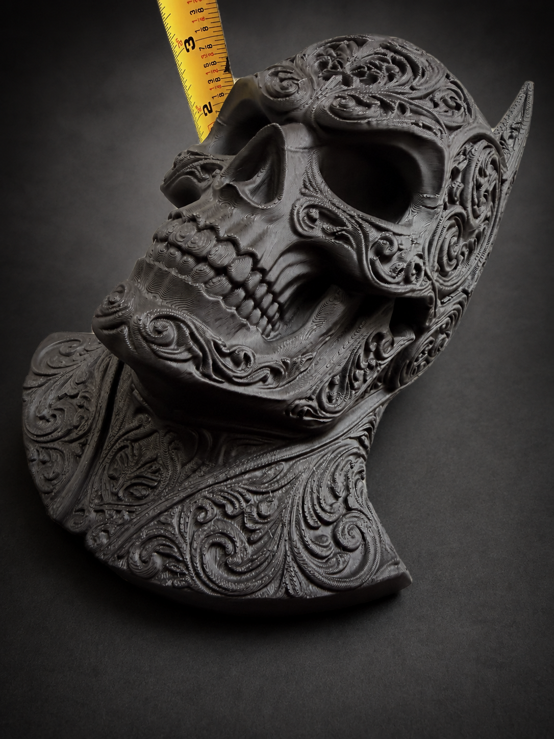 Angled view of the Batman skull beside a tape measure showing the depth of its sculpted face and decorative base.