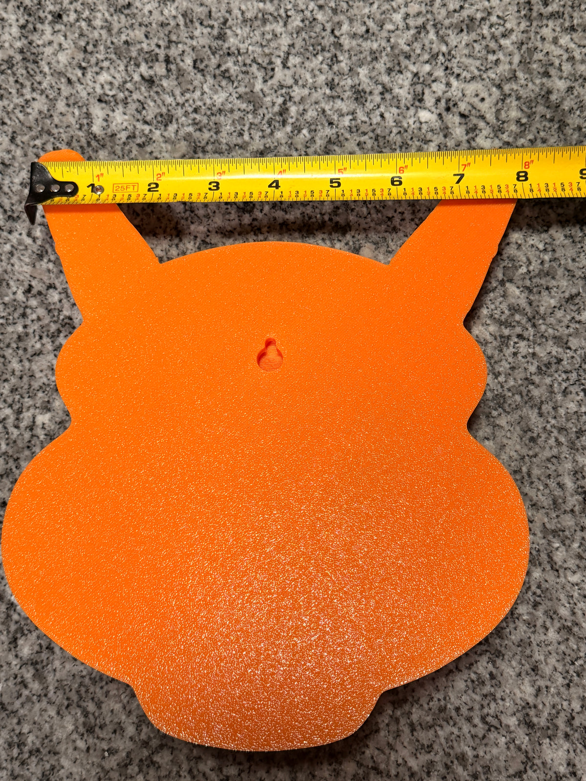 Back of the orange Charizard plaque showing its built-in keyhole hanging slot and a horizontal tape measure.