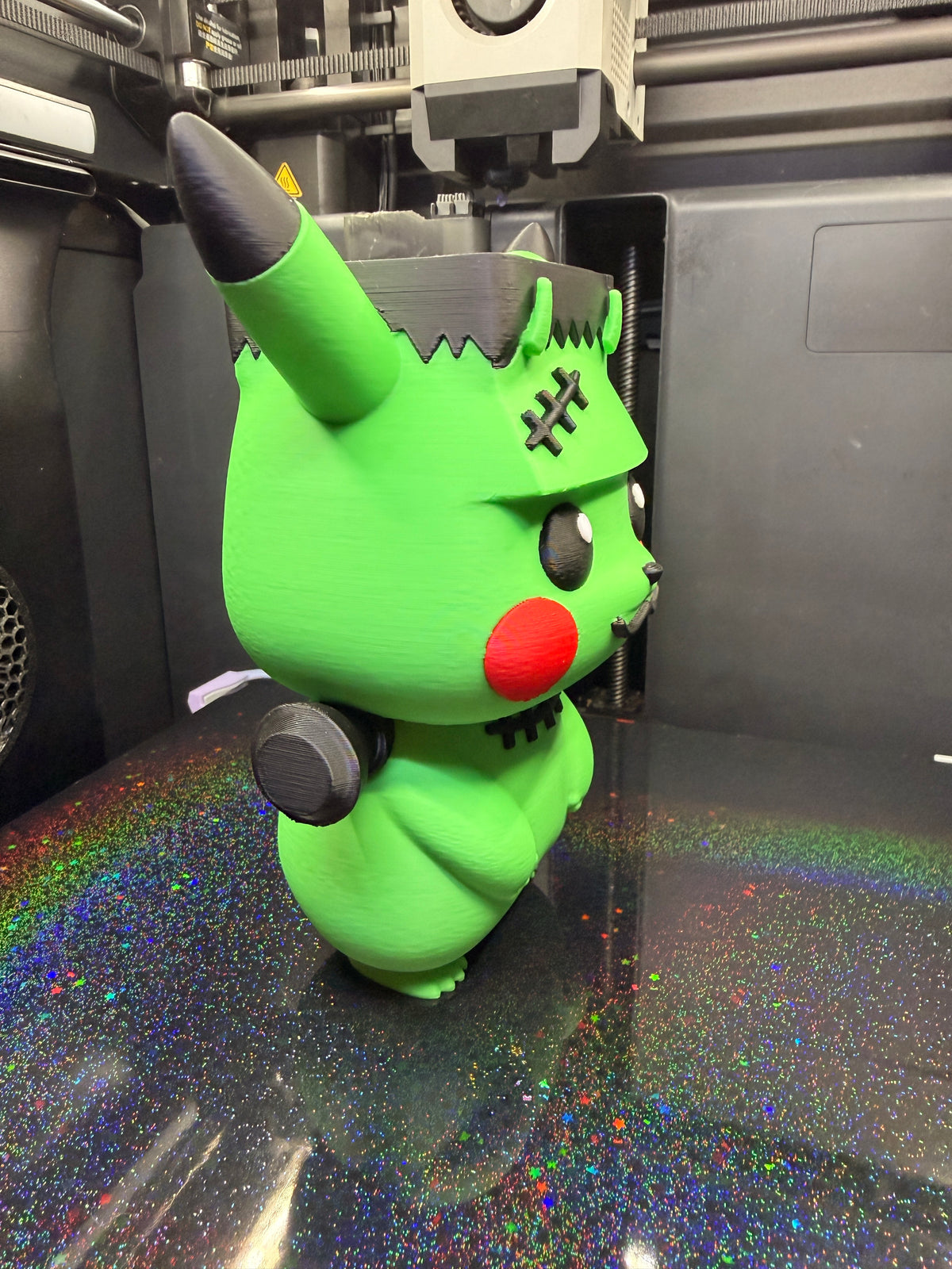 Angled view of Frankenstein Pikachu showing its green body, black-tipped ear, red cheek, and neck bolt.