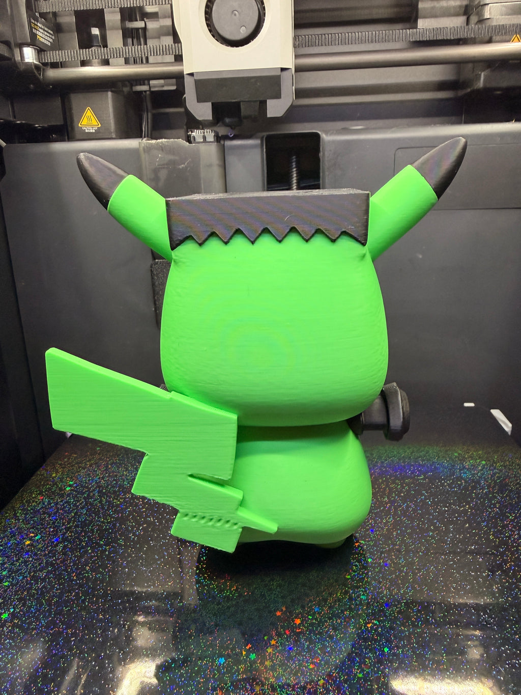 Rear view of Frankenstein Pikachu showing its green lightning-shaped tail, black hair, and ears.