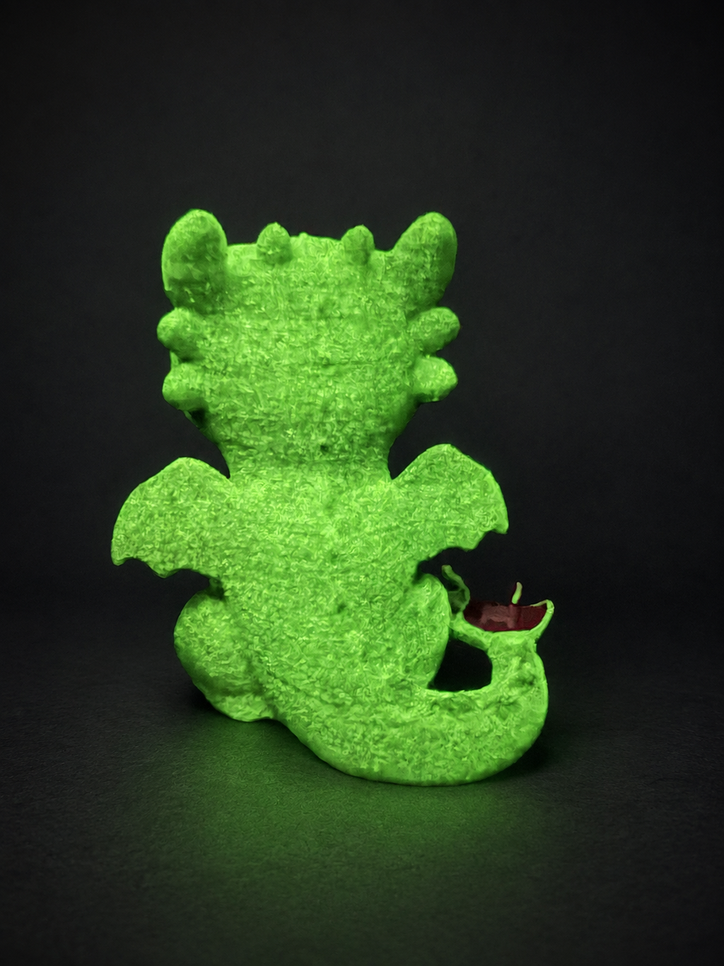 Rear view of the glow-in-the-dark Toothless body glowing green against a dark background, showing wings and curled tail.