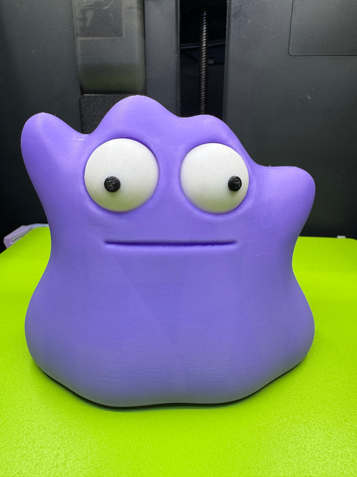 Front view of purple Googly-Eyed Ditto with large movable white eyes and black pupils on a green printer plate.