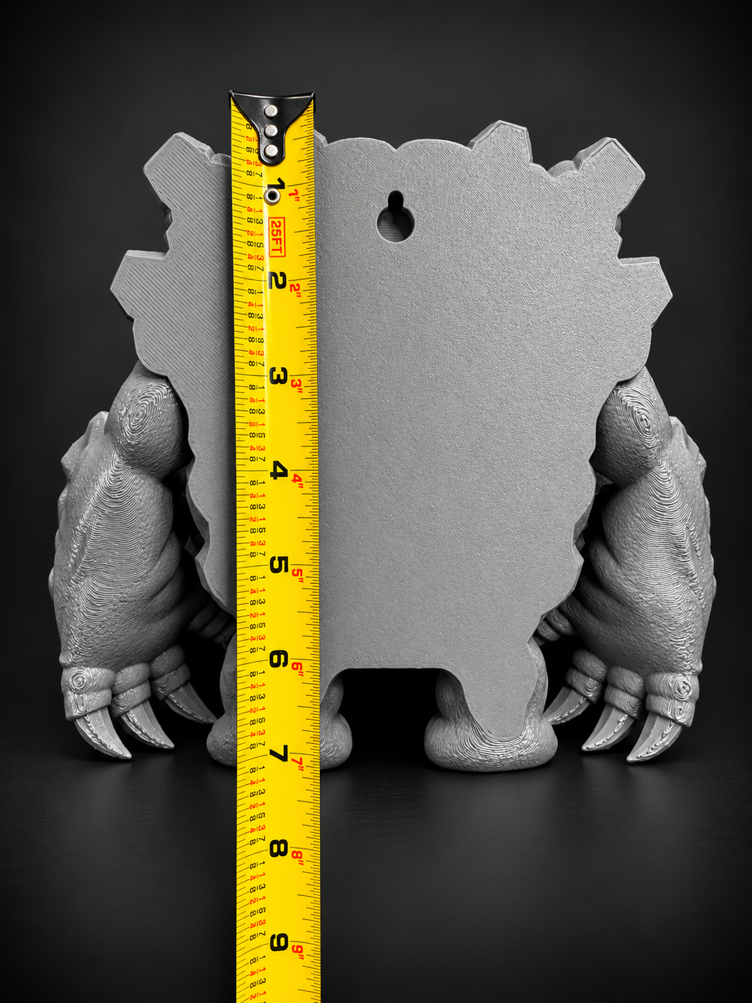 Rear view of gray Graveler wall art showing its built-in keyhole mounting slot and a yellow tape measure for height reference.