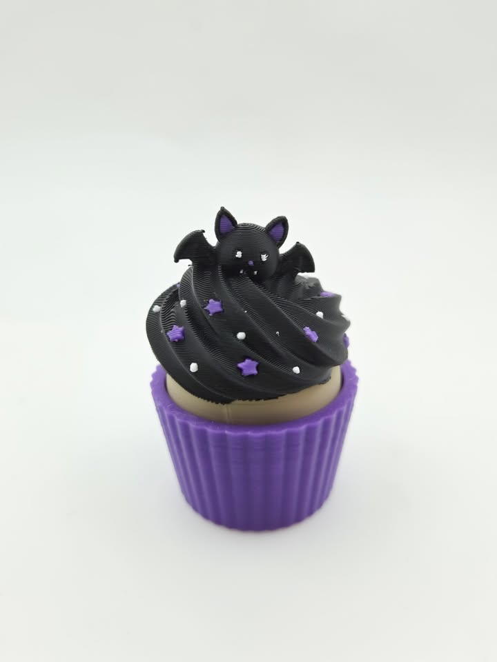 Black decorative cupcake with bat topper, purple stars and purple wrapper.