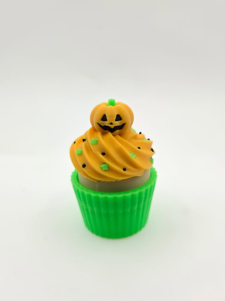 Orange decorative cupcake with jack-o-lantern topper and green wrapper.