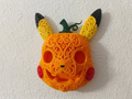 Halloween Pikachu pumpkin wall art mounted on a white wall, with orange filigree, yellow and black ears, red cheeks, and a green stem.