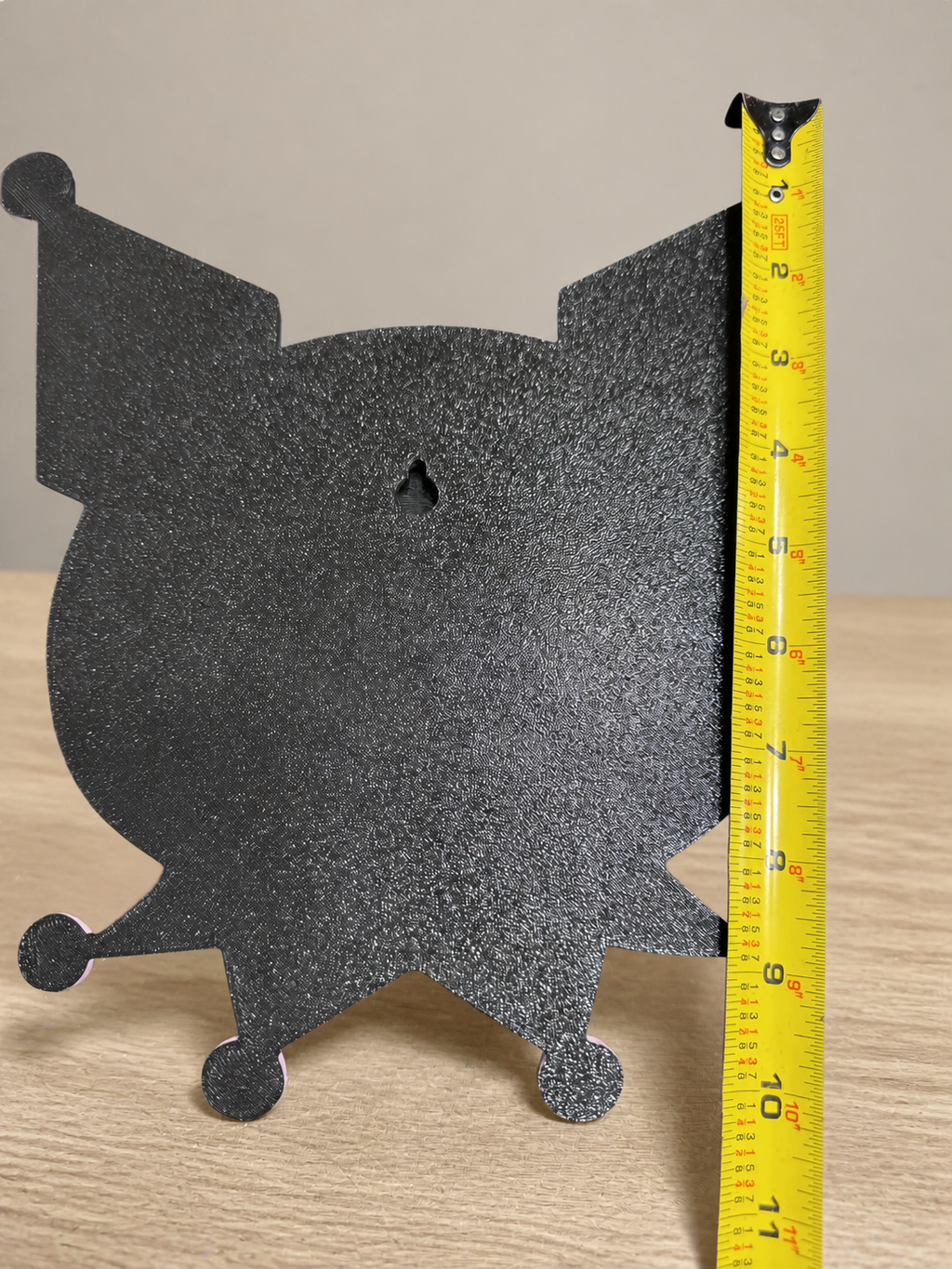 Black back of Kuromi wall art showing a keyhole hanging slot beside a vertical tape measure.