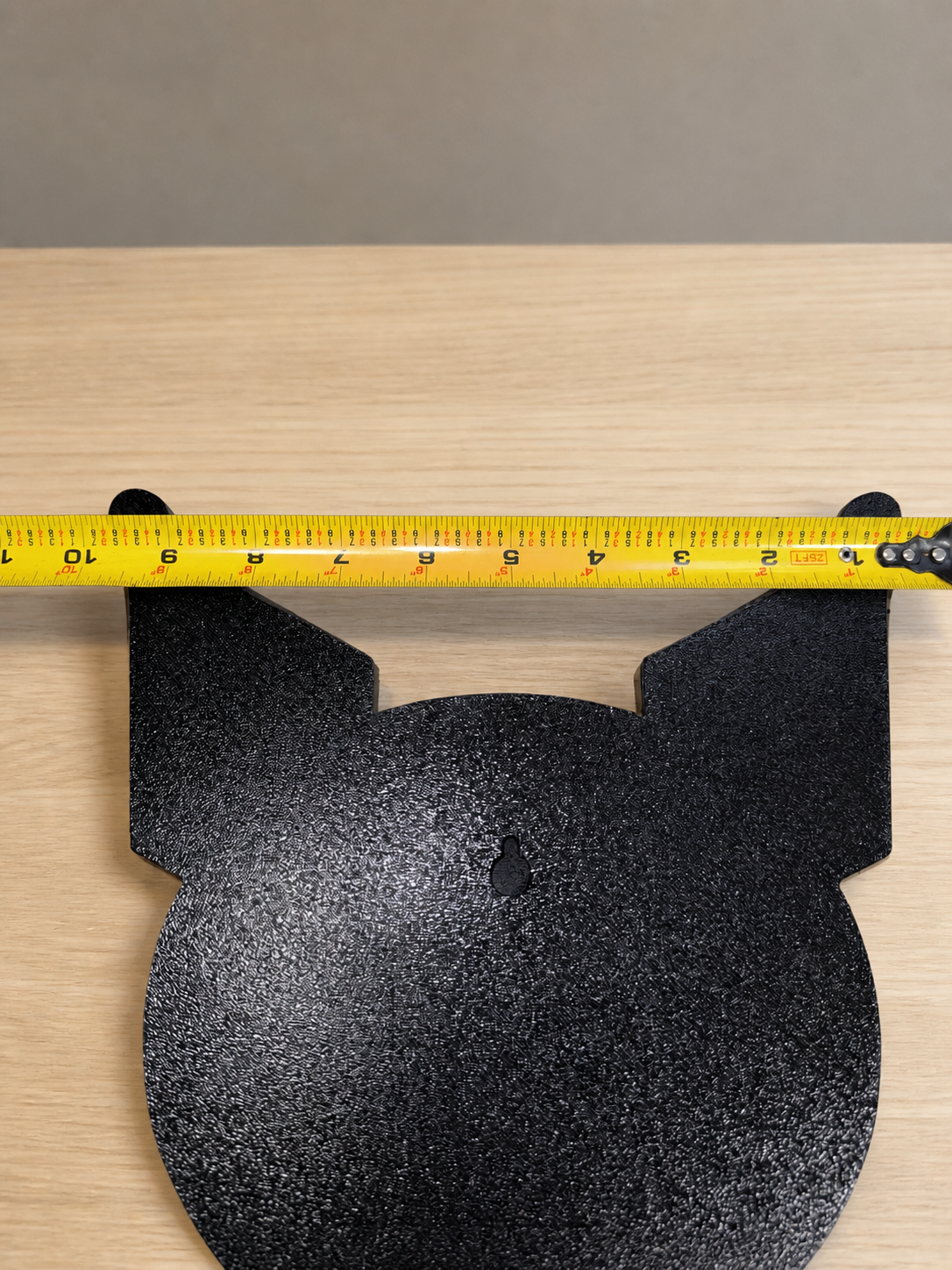 Back of Kuromi wall art with a keyhole slot and a tape measure spanning the pointed ears to show its width.