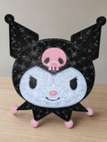 Front of black, white, and pink Kuromi wall art with raised filigree, a pink skull, and pink accents on a wood tabletop.