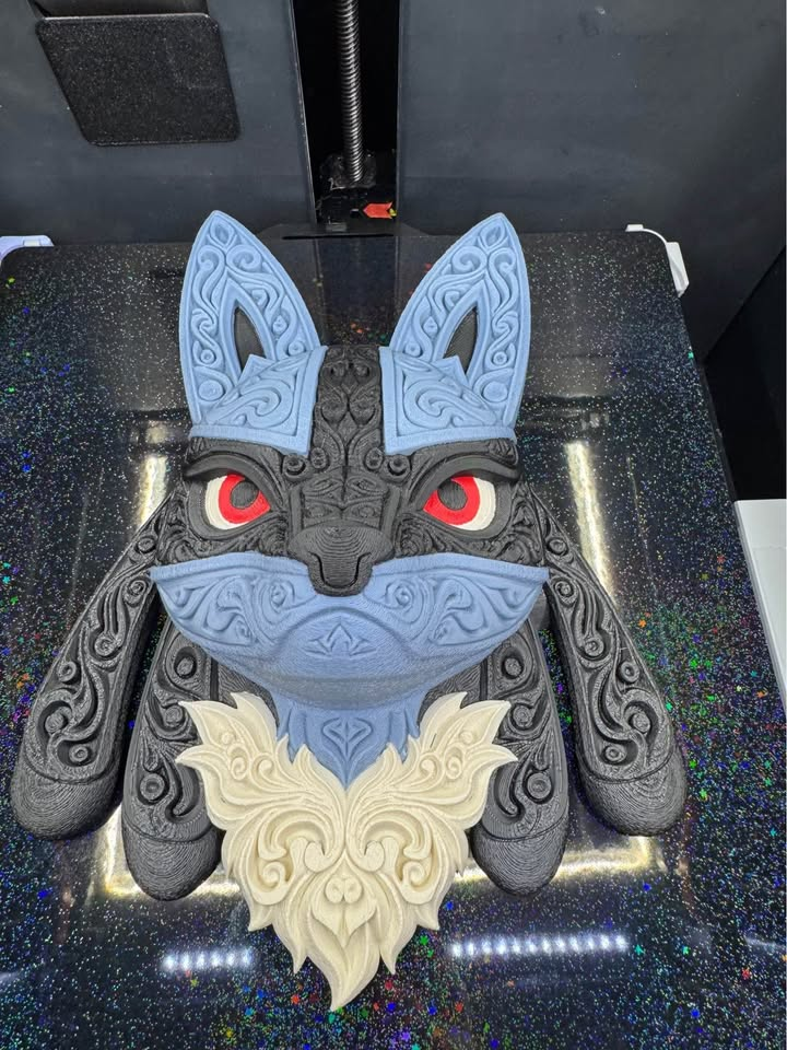 Lucario wall art with raised blue and black filigree, red eyes, and a cream chest accent resting on a 3D printer bed.