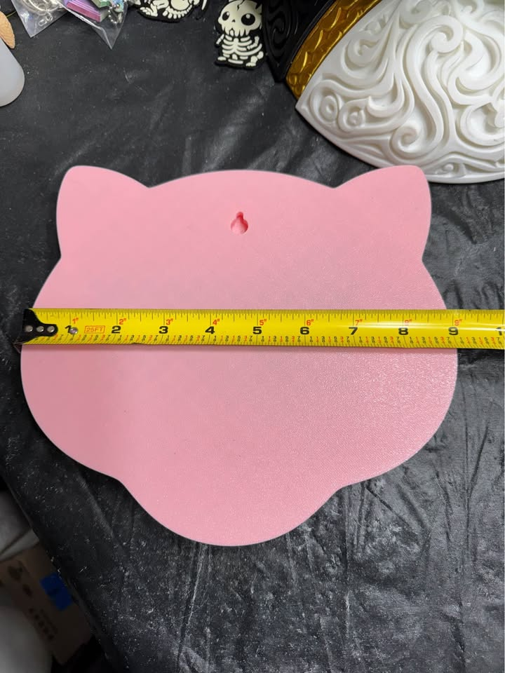 Pink back of Mew wall art with a keyhole hanging slot and a horizontal tape measure across its width.