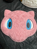 Pink Mew wall art with ornate raised filigree, blue and white eyes, and black pupils on a dark work surface.