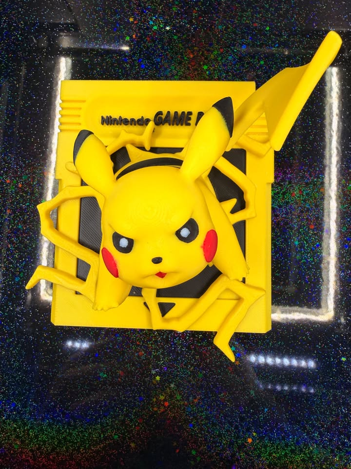 Yellow Pikachu emerging from a yellow Game Boy cartridge-style wall plaque with black details, red cheeks, and raised lightning bolts.