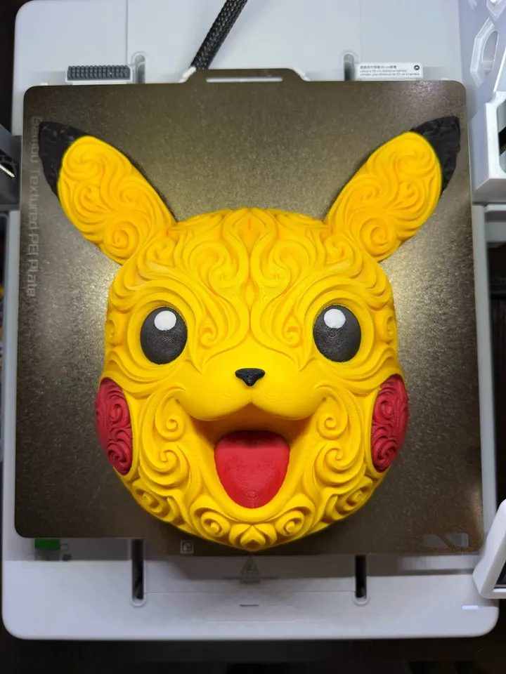 Yellow Pikachu head wall art showing raised filigree, black ear tips and eyes, red cheeks, and a smiling mouth on a printer plate.