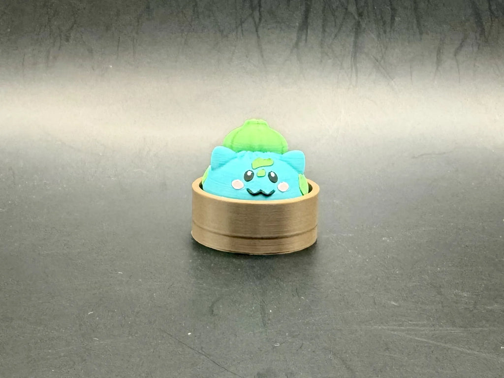 Turquoise Bulbasaur dumpling clicker with a green bulb and spots in a brown steamer-style base.