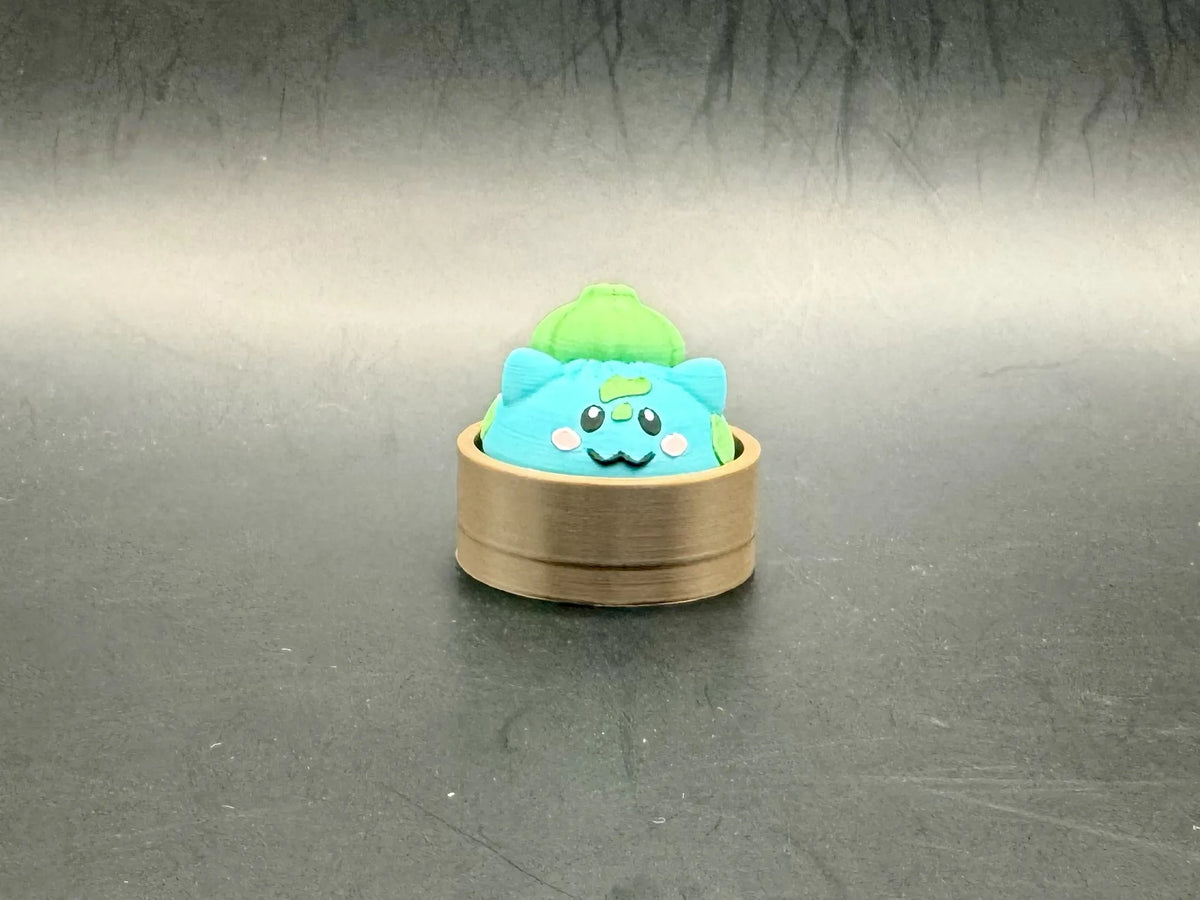 Turquoise Bulbasaur dumpling clicker with a green bulb and spots in a brown steamer-style base.
