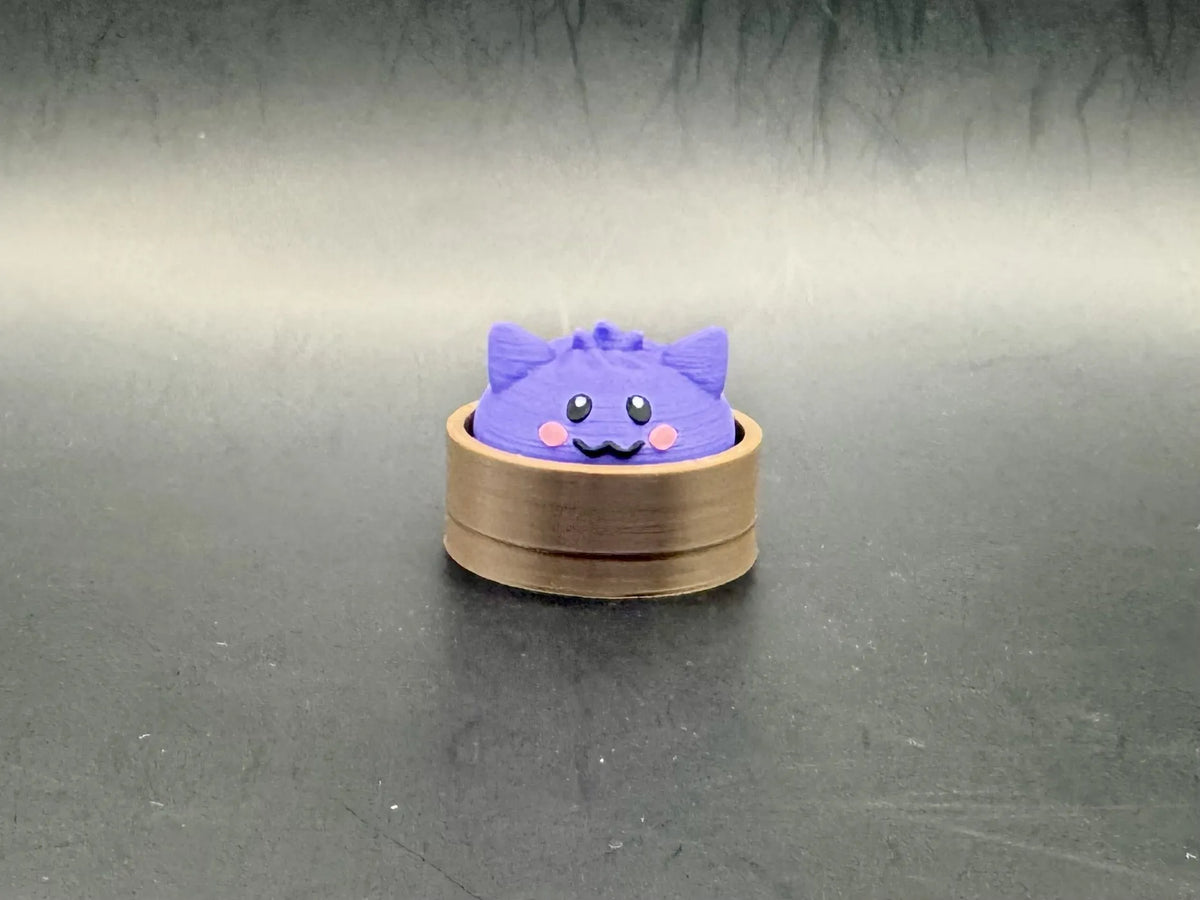 Purple Gengar dumpling clicker with pointed ears and pink cheeks in a brown steamer-style base.