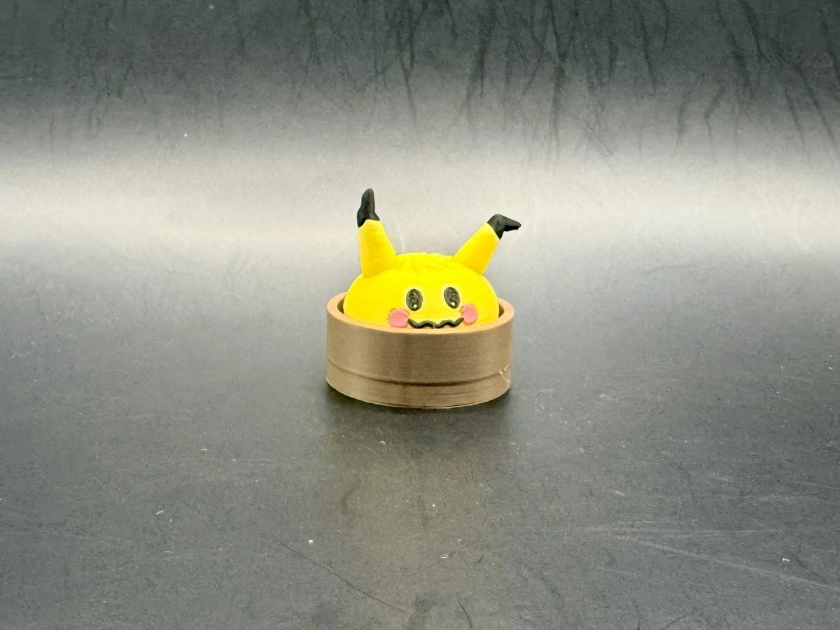 Yellow Mimikyu dumpling clicker with bent black-tipped ears in a brown steamer-style base.