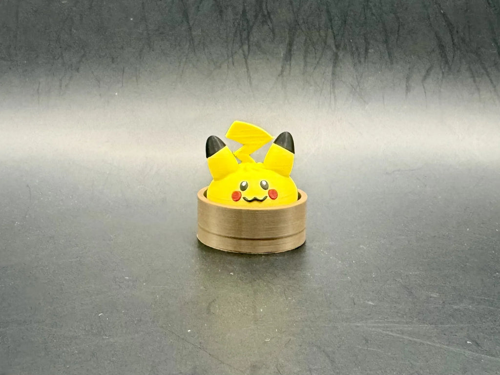 Yellow Pikachu dumpling clicker with black ear tips, red cheeks, and a lightning-bolt tail in a brown steamer-style base.