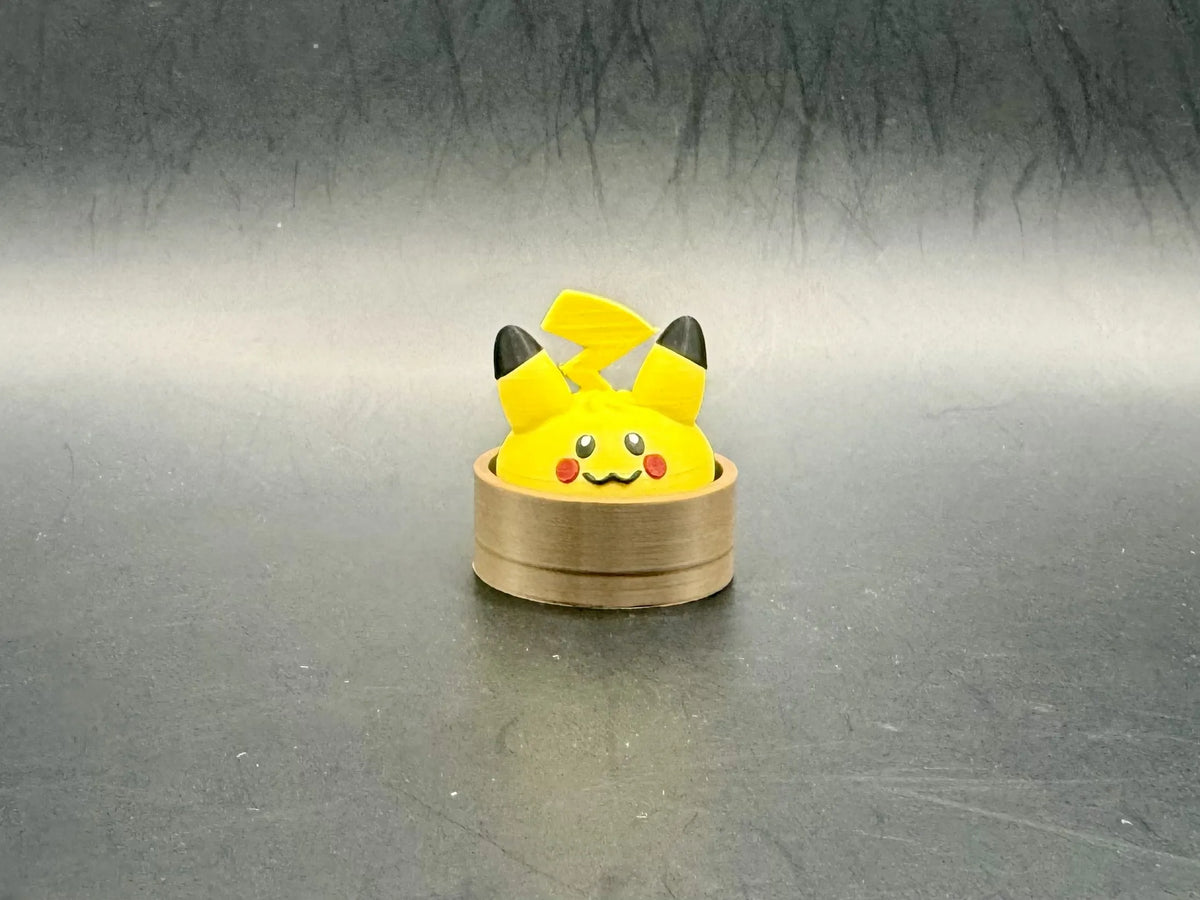 Yellow Pikachu dumpling clicker with black ear tips, red cheeks, and a lightning-bolt tail in a brown steamer-style base.