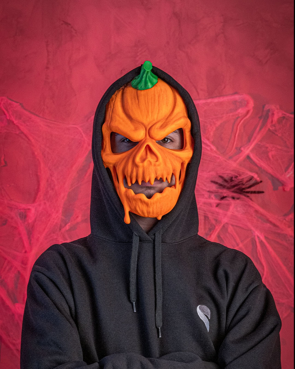 Front fit example of a person wearing the orange and green pumpkin Halloween mask with a black hood.