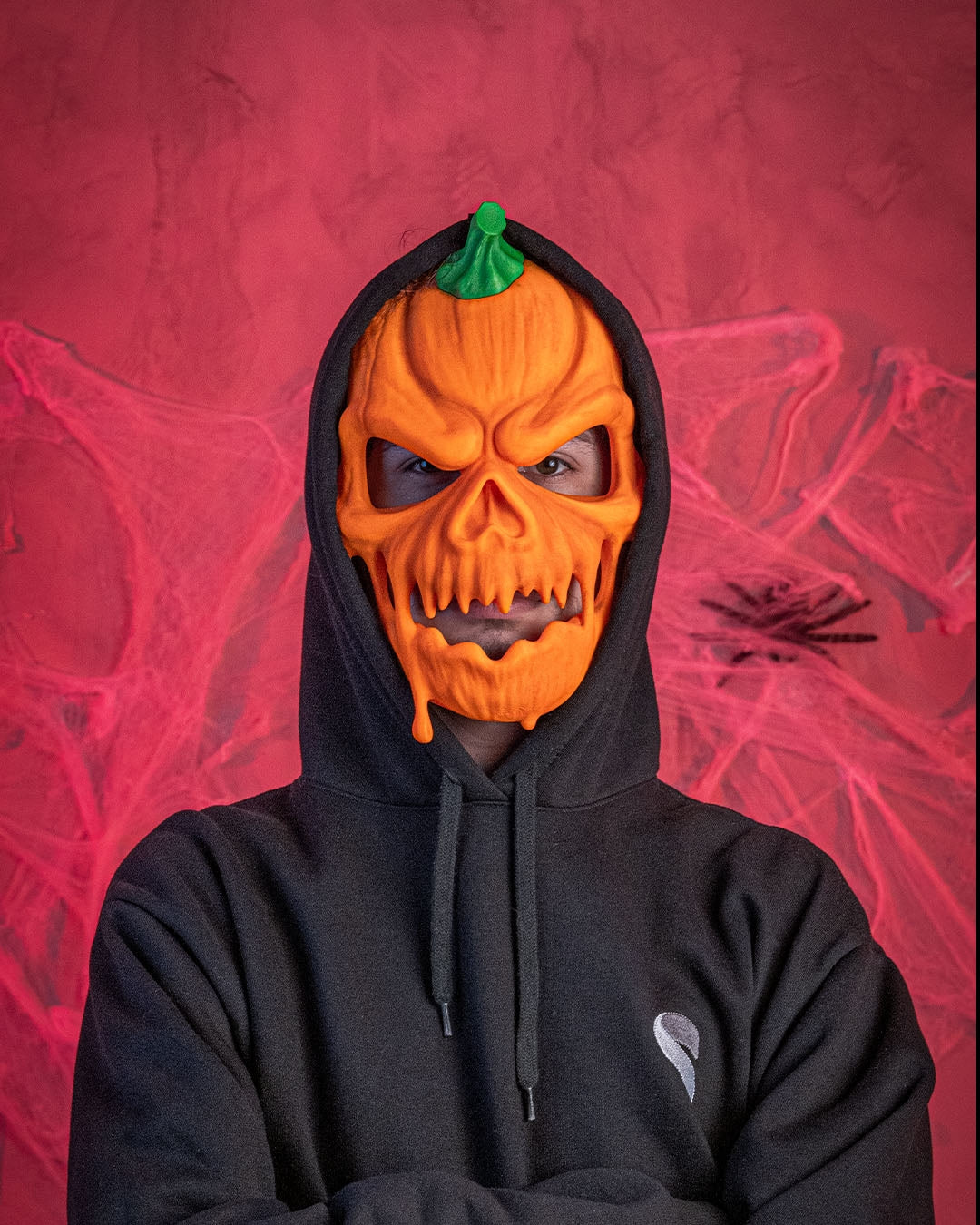 Front fit example of a person wearing the orange and green pumpkin Halloween mask with a black hood.