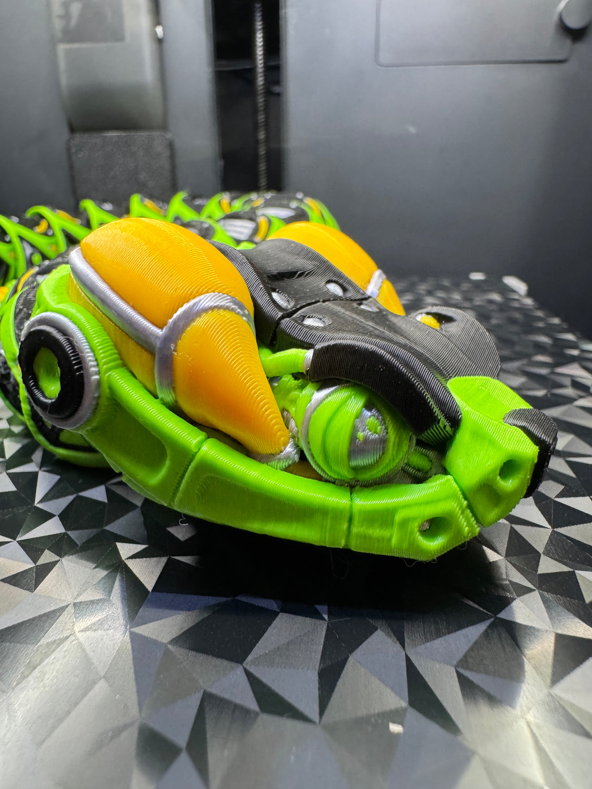 Three-quarter close-up of the robotic snake head showing yellow side accents and silver mechanical details.