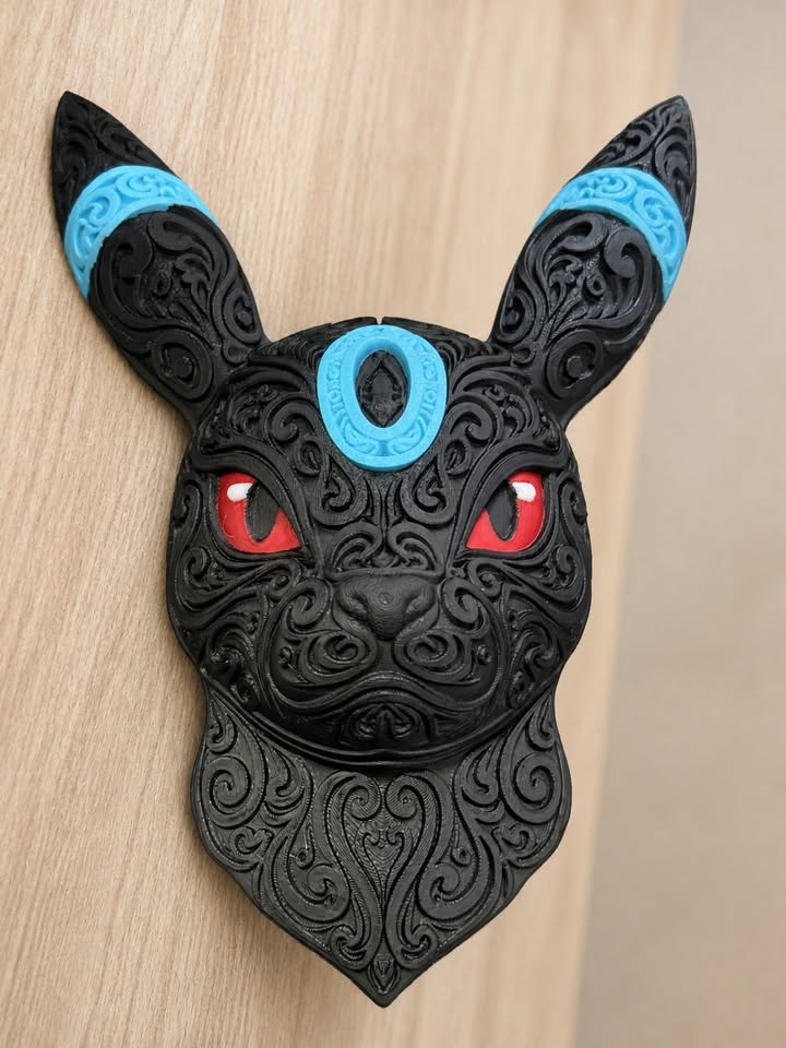 Black Shiny Umbreon wall art with raised filigree, blue forehead and ear rings, and red eyes against a wood background.