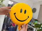 Yellow 3D printed smiley balloon with black eyes and smile, held upright to show its sculpted balloon edge.