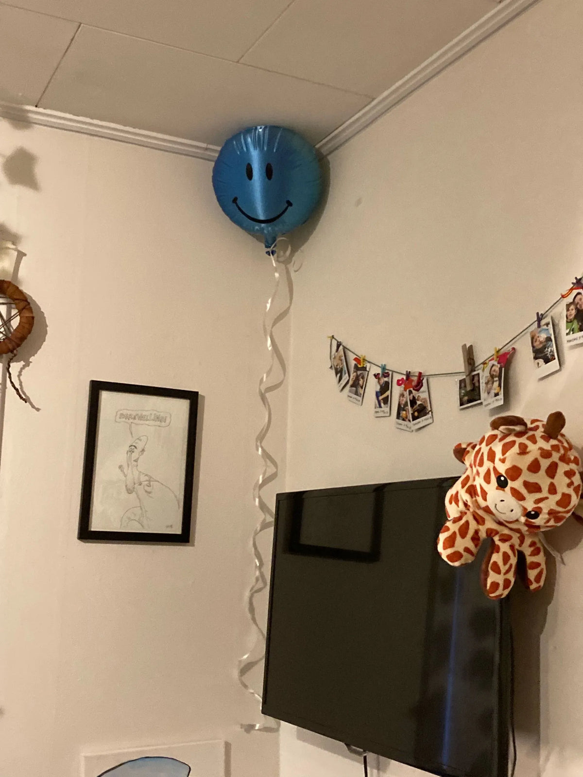 Blue smiley balloon with black face mounted high on a bedroom wall with a white curling ribbon.