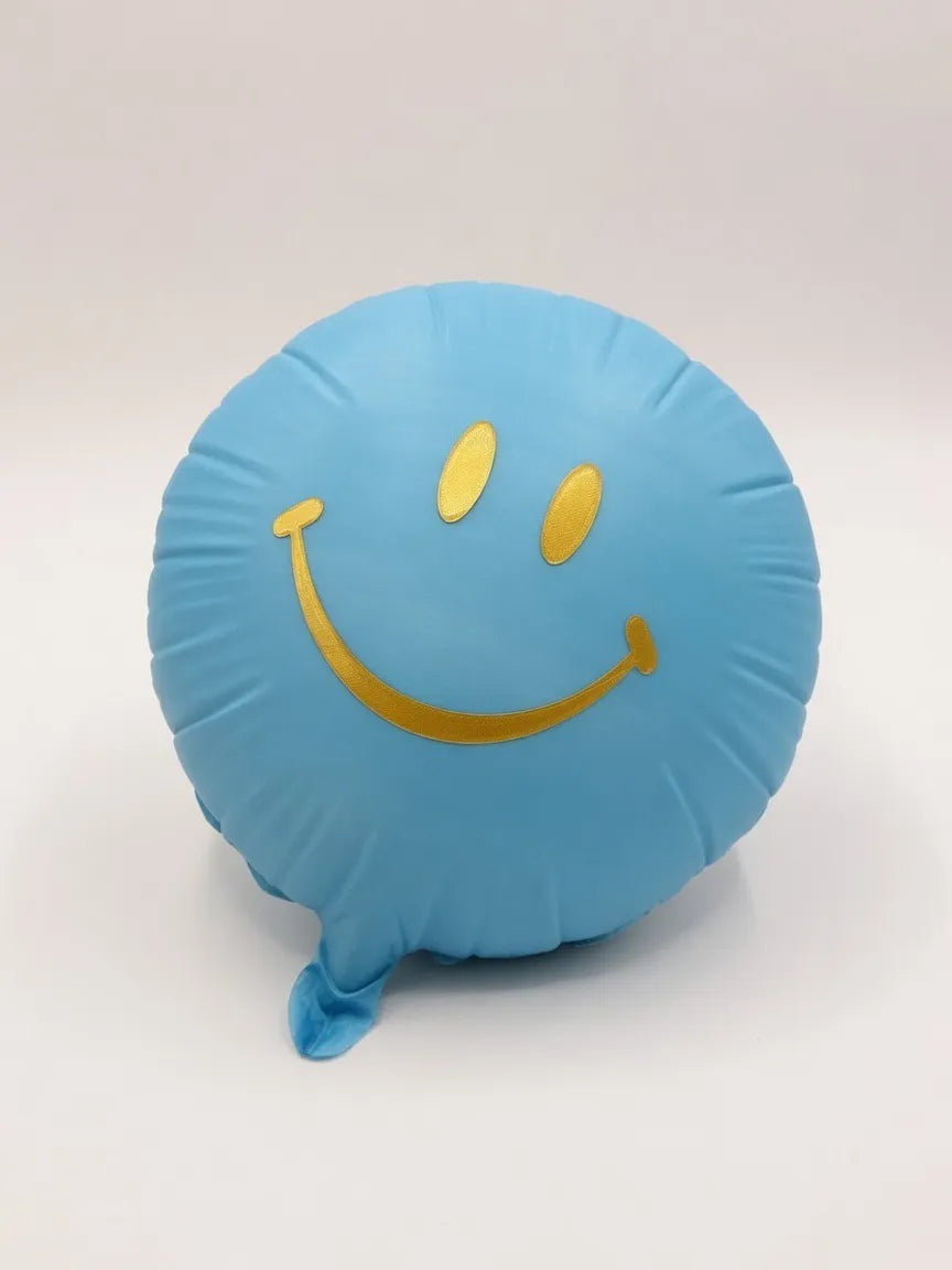 Light blue smiley balloon with gold-colored eyes and smile against a white background.