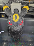 Black Umbreon wall art with ornate raised filigree, yellow forehead and ear rings, and red eyes upright on a 3D printer bed.
