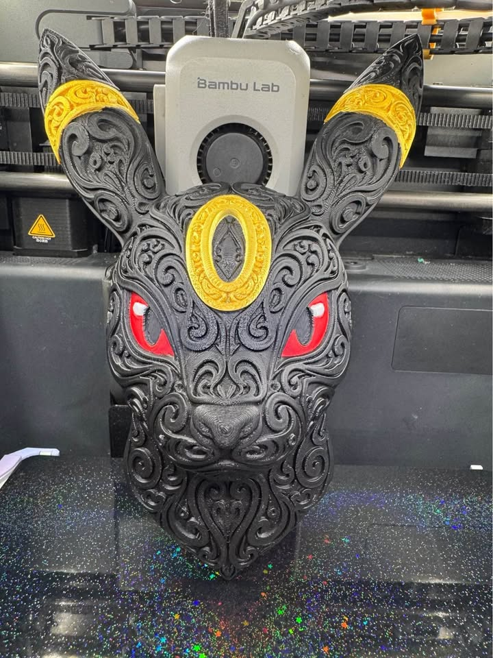 Black Umbreon wall art with ornate raised filigree, yellow forehead and ear rings, and red eyes upright on a 3D printer bed.