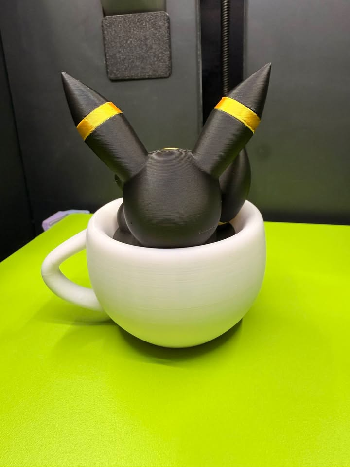 Rear view of a black Umbreon figure with gold ear rings resting inside a white decorative teacup.