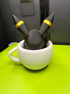 Rear view of a black Umbreon figure with gold ear rings resting inside a white decorative teacup.