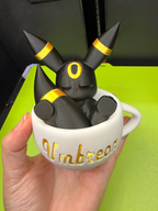 Umbreon teacup figurine held in a hand to show scale, with a sleeping black Umbreon, gold rings, and a white cup.